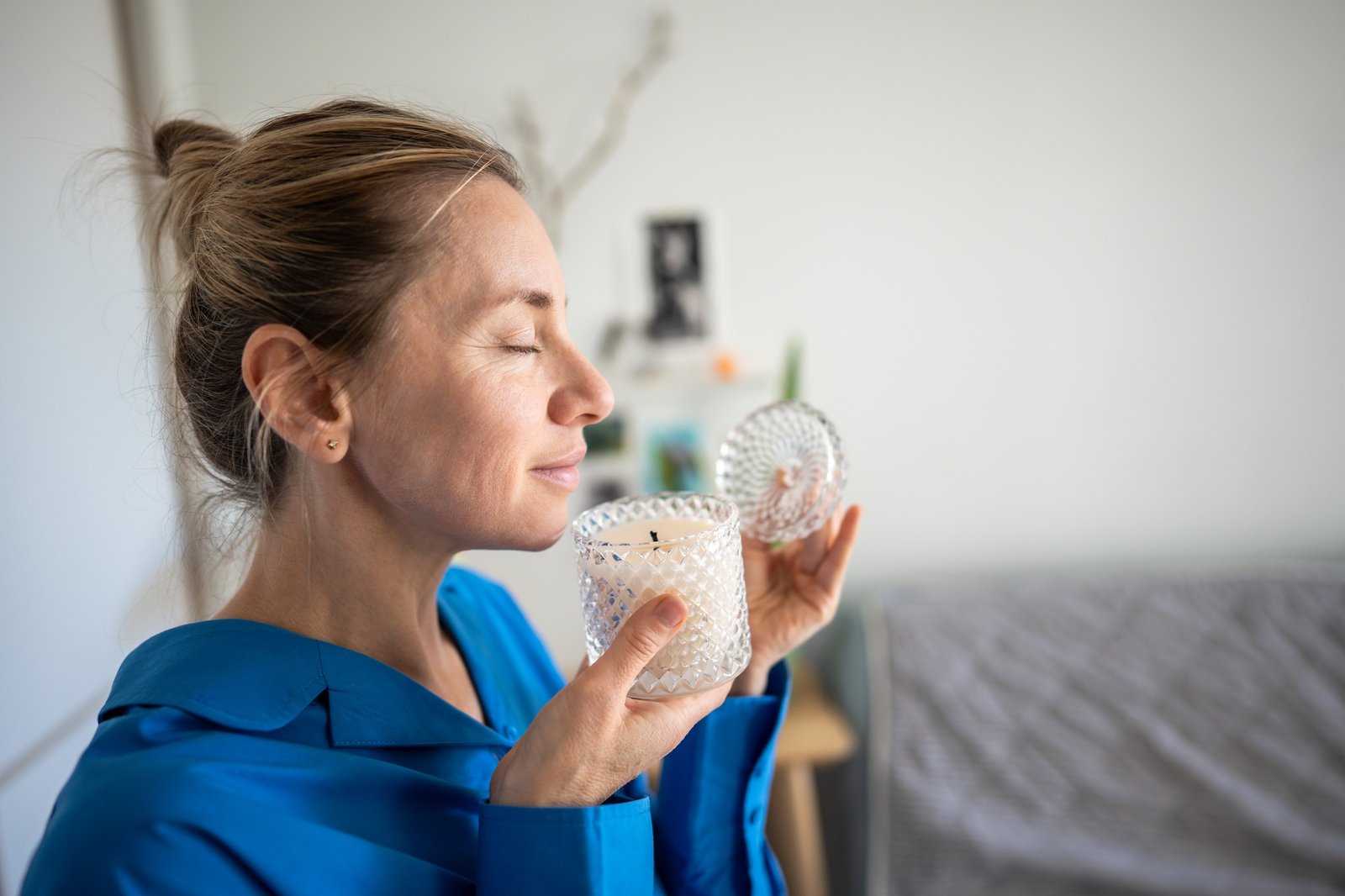 Aromatherapy for inner peace of middle aged woman smelling aromatic candle with closed eyes at home.